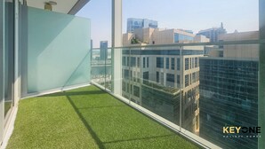 A balcony with artificial grass, large windows, and a cityscape view. - Majestine Stylish Studio with Canal View (Dubai)