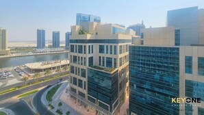 A modern high-rise building with a glass facade, located near a waterfront with a road and parking area. - Majestine Stylish Studio with Canal View (Dubai)