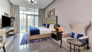 A modern hotel room with a large bed, a desk, a chair, a small table, and a TV. - Majestine Stylish Studio with Canal View (Dubai)