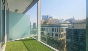A balcony with artificial grass, large windows, and a cityscape view.