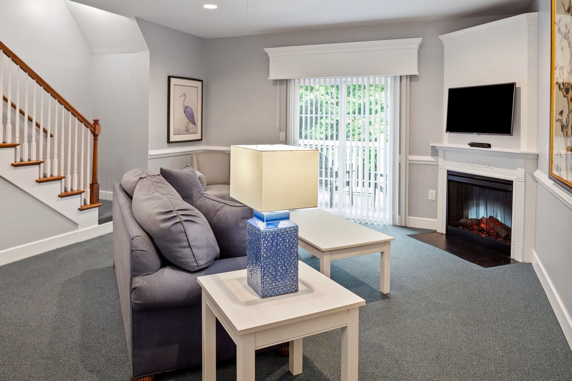 A living room with a grey sofa, a white coffee table with a blue vase, a fireplace, and a TV mounted above it.