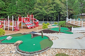Un campo de mini golf con una estructura roja para jugar y una valla blanca.