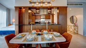 Een eetgedeelte met een tafel voor zes personen, een keuken op de achtergrond, en een bed met blauw beddengoed aan de linkerzijde.