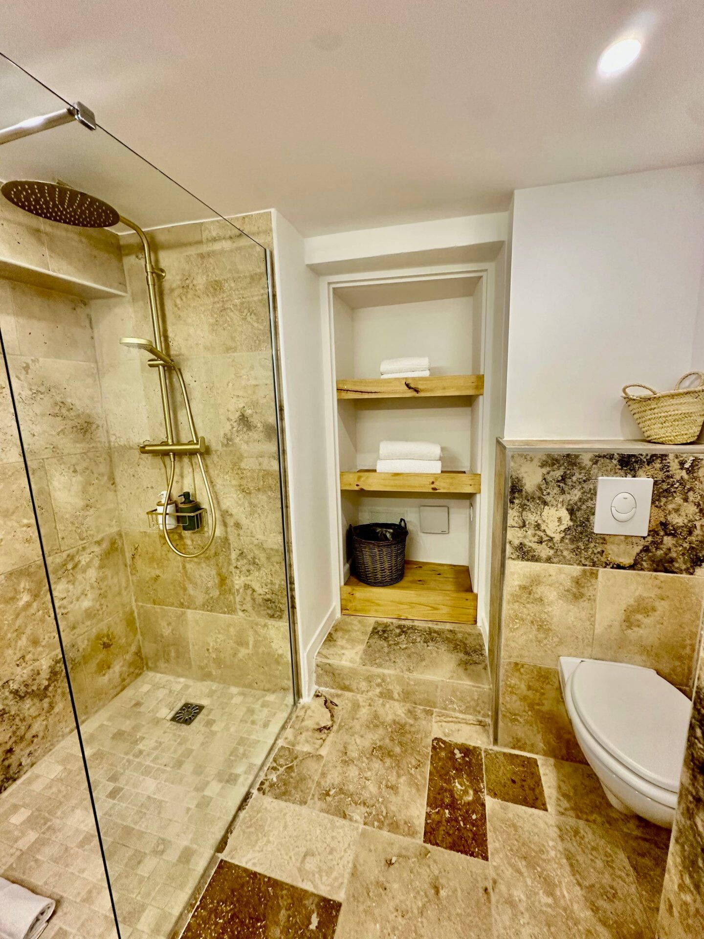 A bathroom with a glass-enclosed shower, a toilet, and shelves with towels.