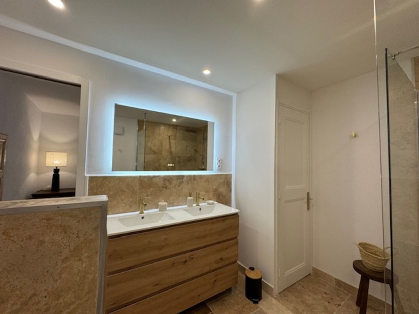 A modern bathroom with a large mirror, two sinks, a wooden vanity, and a glass shower enclosure.
