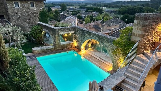 A pool area with a stone bridge, surrounded by greenery and stone buildings. - Le Clos du Vialle (Grillon)