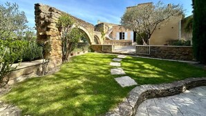 A courtyard with stone ruins, a paved walkway, and a building with a tiled roof. - Le Clos du Vialle (Grillon)