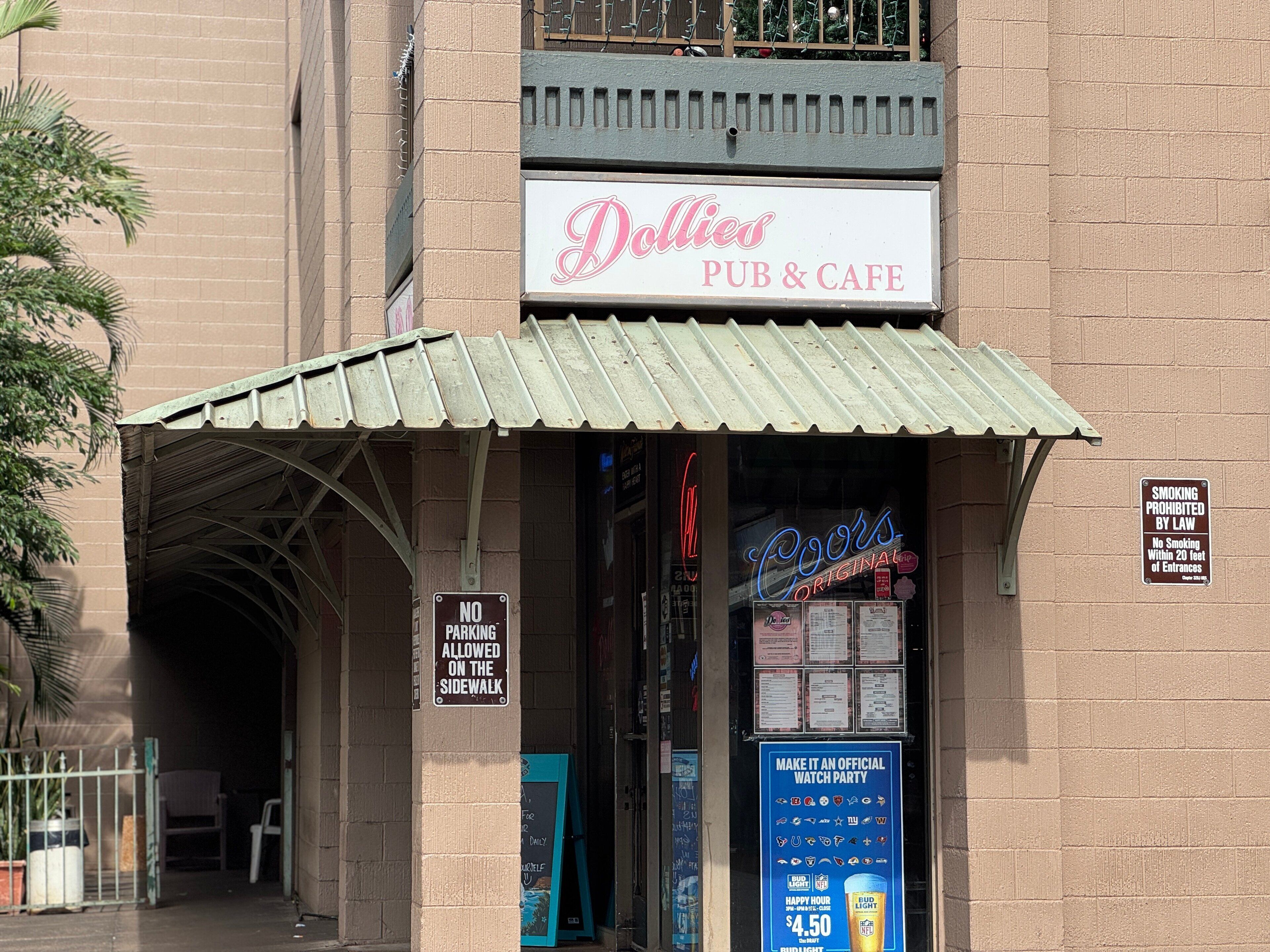 Eine Kneipe und ein Café namens 'Dollies' mit einer Neonreklame, einem 'Parkverbot'-Schild und einem 'Rauchen verboten'-Schild.