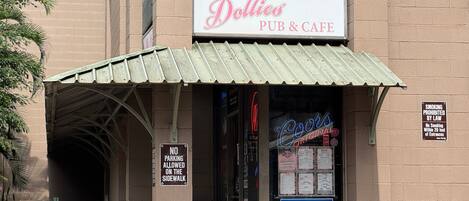 Eine Kneipe und ein Café namens 'Dollies' mit einer Neonreklame, einem 'Parkverbot'-Schild und einem 'Rauchen verboten'-Schild.