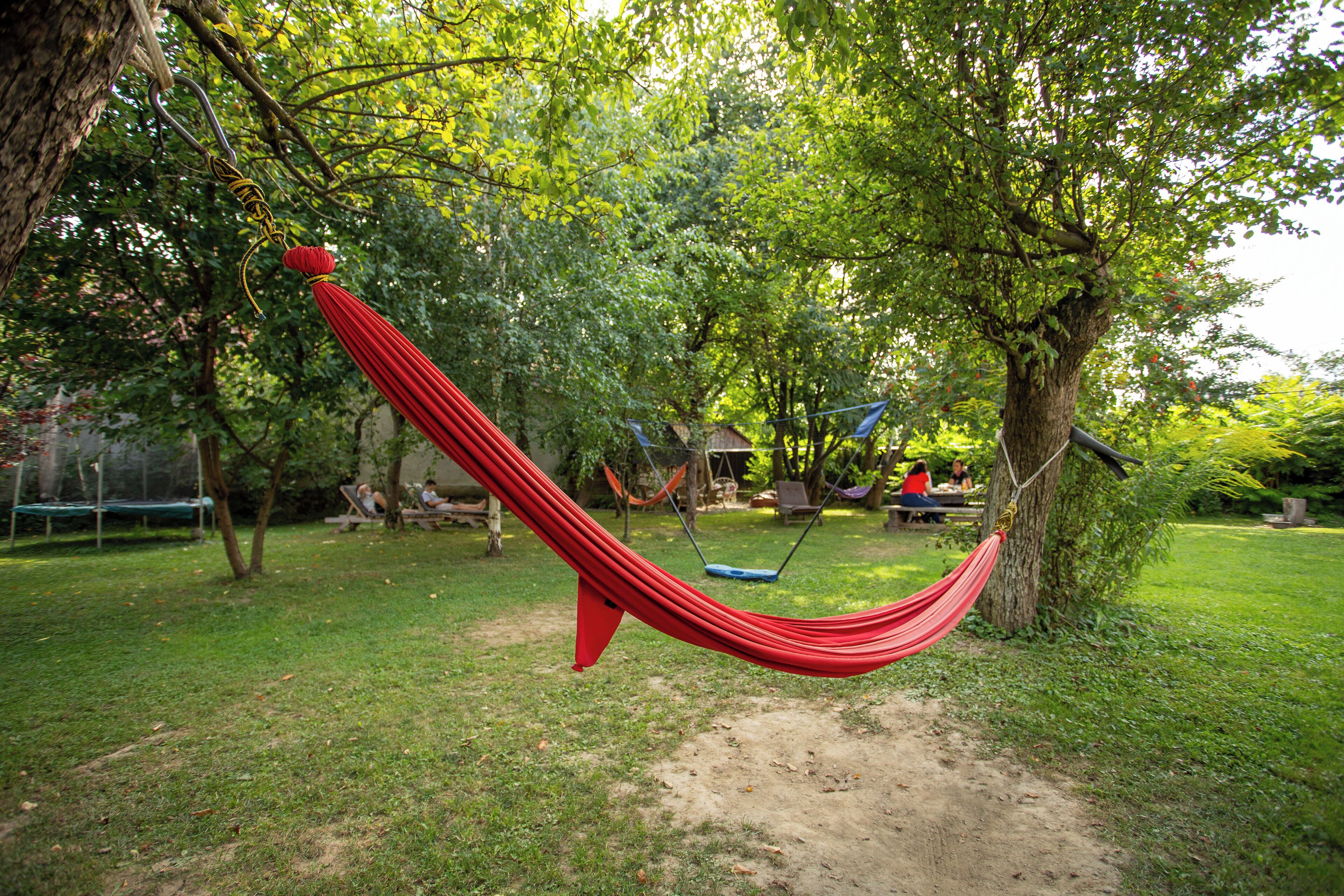 A hammock suspended between trees in a grassy area with a swing set and picnic table in the background.