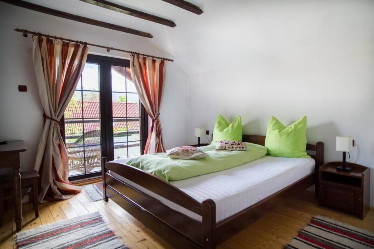 A bedroom with a wooden bed, green pillows, a nightstand, and a window with curtains.