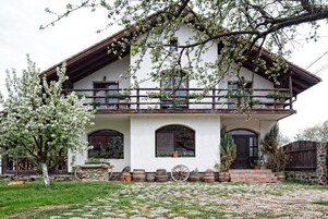 Una casa tradicional de dos pisos con un balcón, escalones de piedra y un jardín con un árbol.
