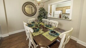 A dining room with a wooden table set for four, white chairs, a mirror, and a chandelier.