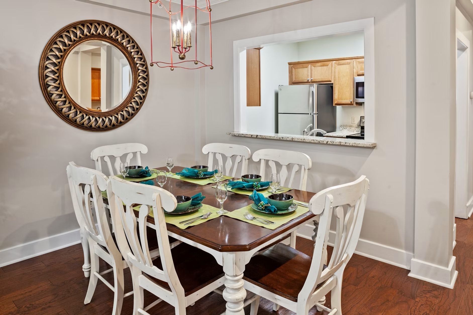Une salle à manger avec une table en bois mise pour six personnes, des chaises blanches et un grand miroir au mur.