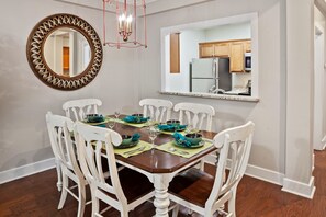 Comedor con una mesa de madera dispuesta para seis comensales, sillas blancas y un espejo grande en la pared.