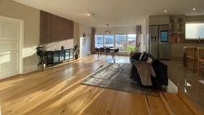 A spacious living area with a wooden floor, a sofa, a dining table with chairs, a kitchen area, and large windows offering a view of the outside. - Exclusive newly apartment with free parking (Västra Götalands län)