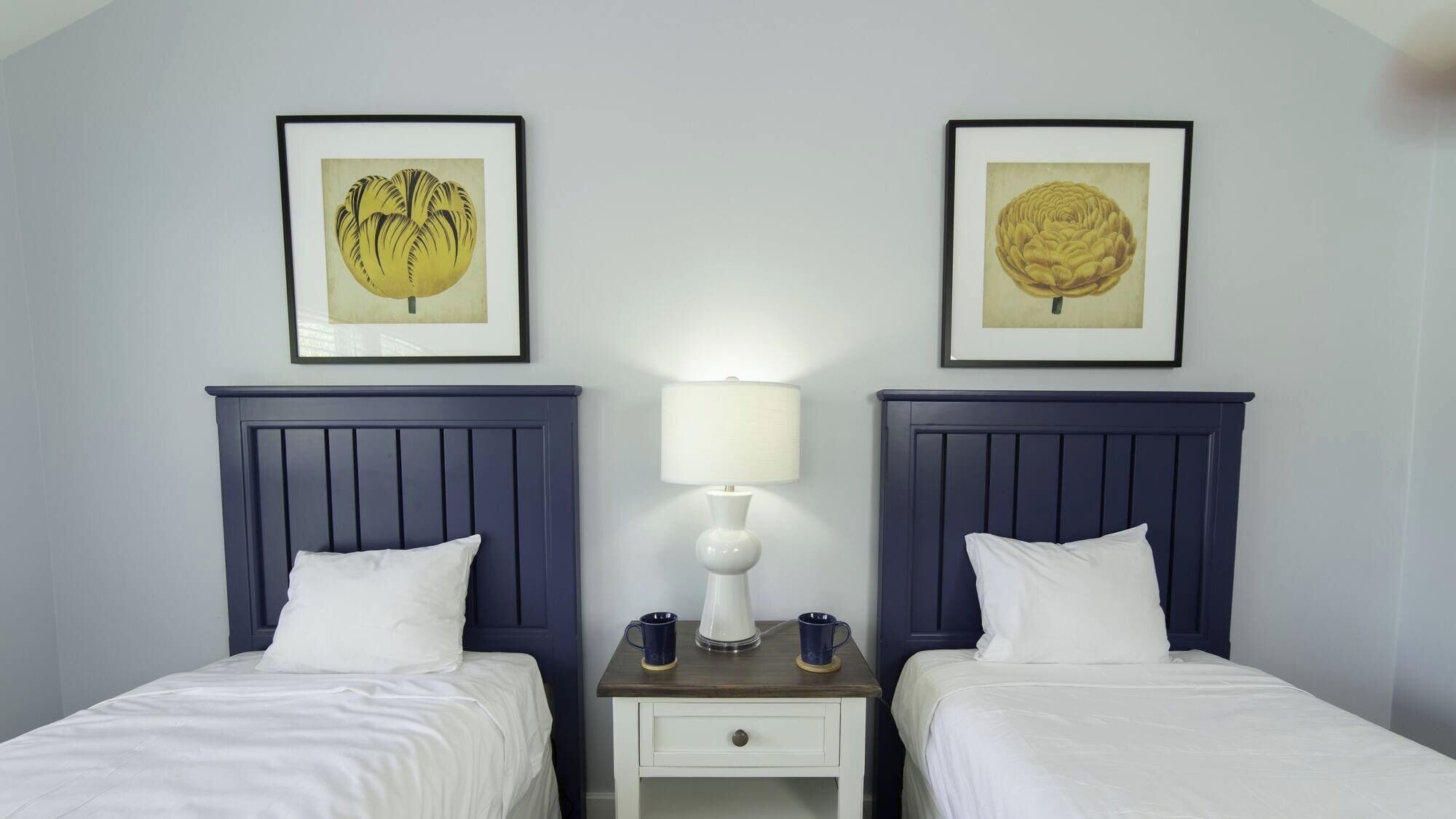 Une chambre d’hôtel avec deux lits, une table de chevet entre les deux, et deux reproductions encadrées de motifs botaniques accrochées au mur.
