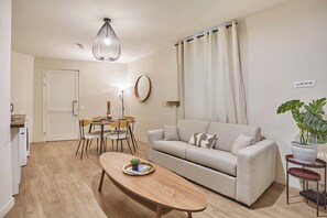 A living room with a sofa, a dining table, a hanging light fixture, a potted plant, and a door. - Apartment Exposition Center (Paris)
