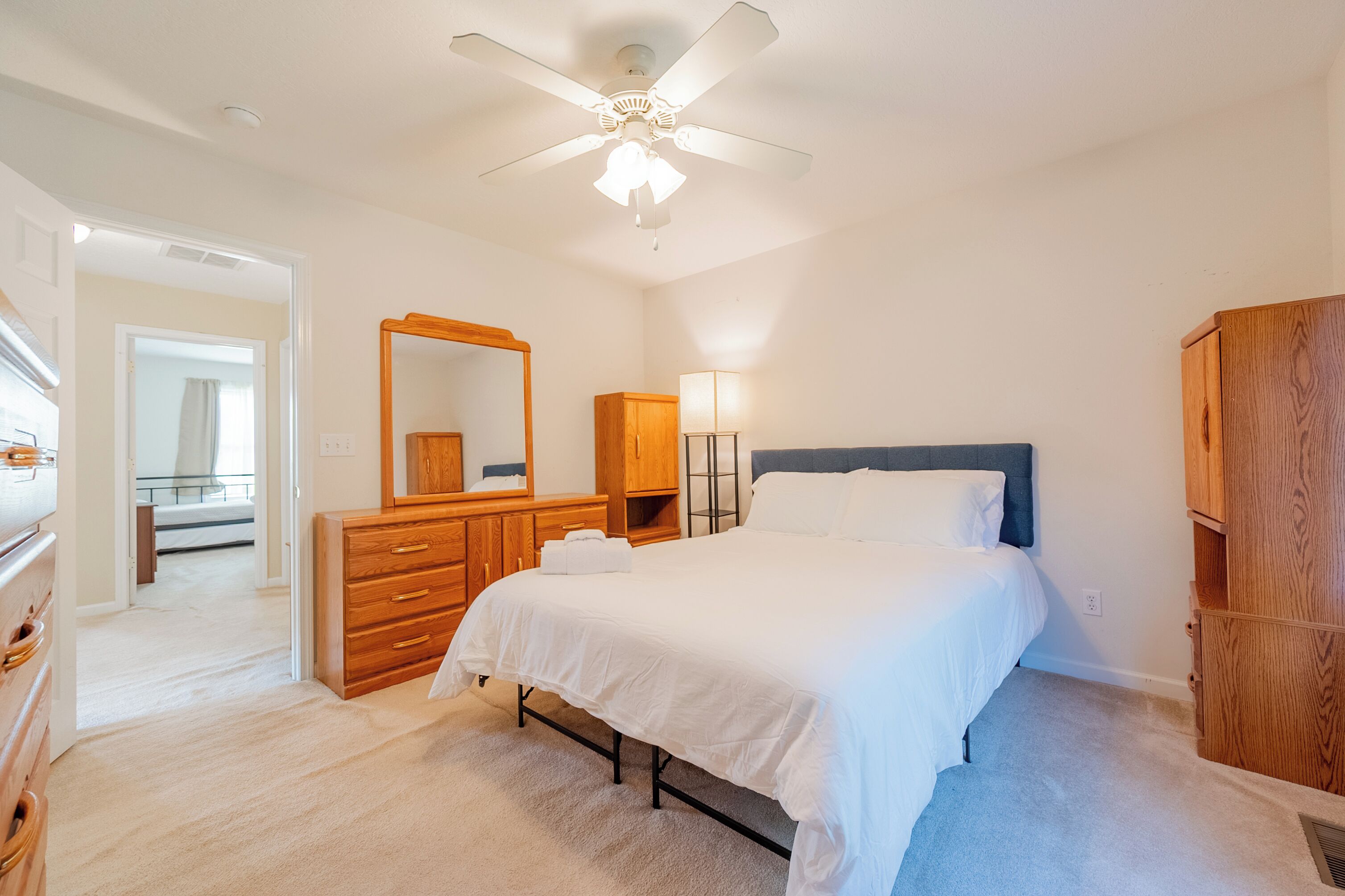 Une chambre à coucher avec un lit, une commode en bois, un miroir et un ventilateur de plafond.