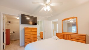 Een slaapkamer met een bed, een houten dressoir en een plafondventilator.