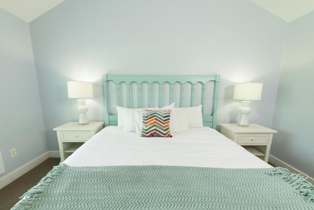 A neatly made bed with a striped pillow, two bedside tables with lamps, and a light blue wall.