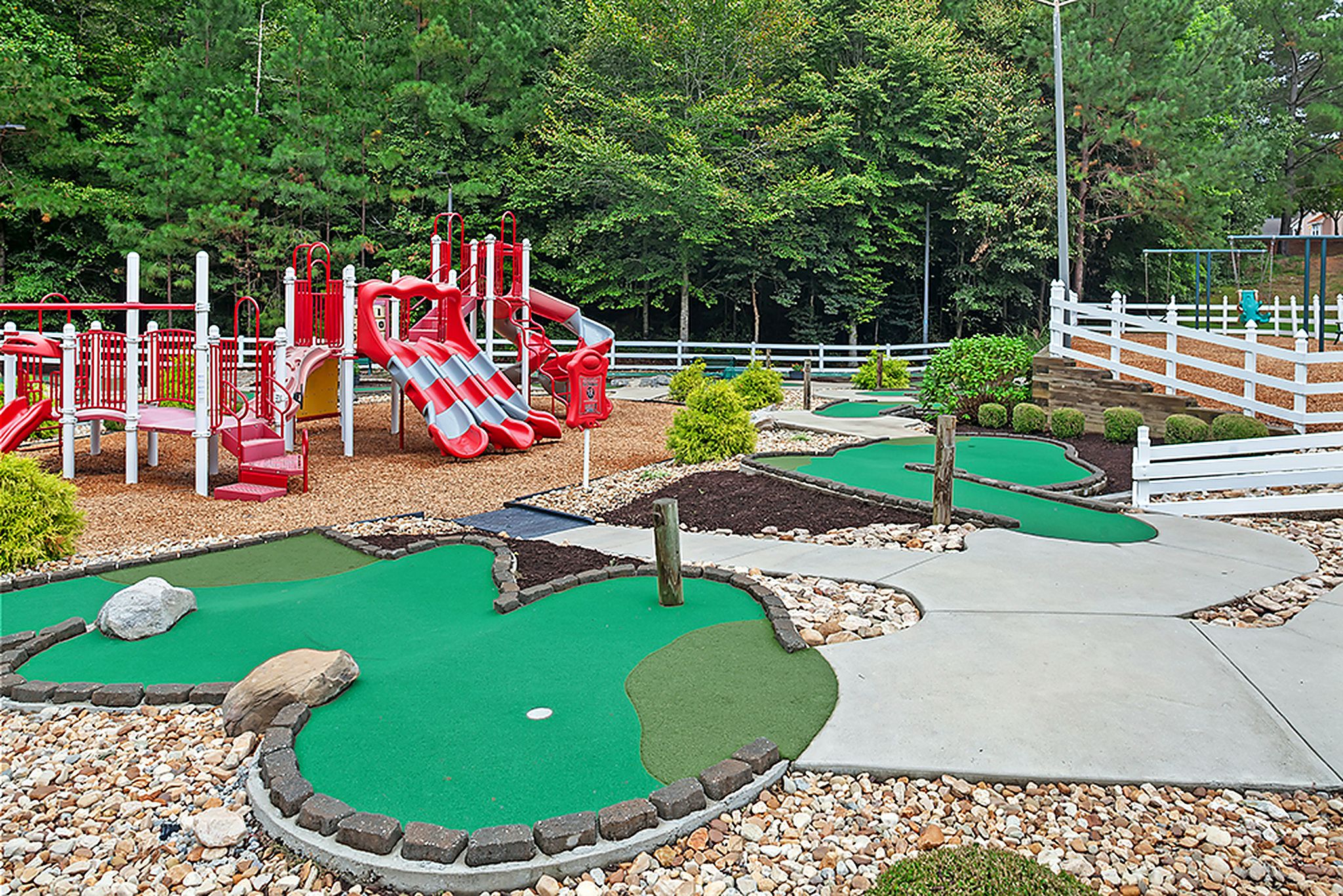 A miniature golf course with a red play structure and a white fence.