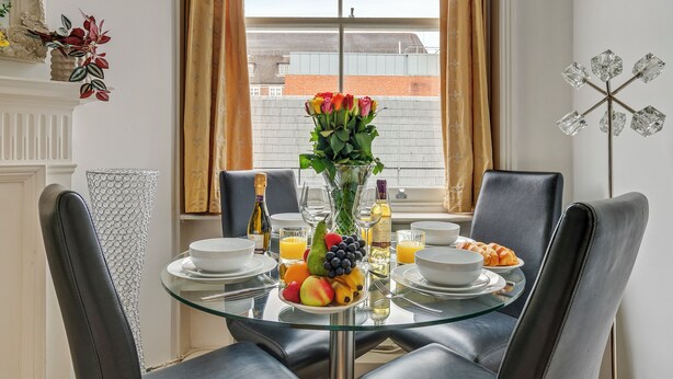 A breakfast table with fruit, a vase of flowers, and a bottle of champagne.
