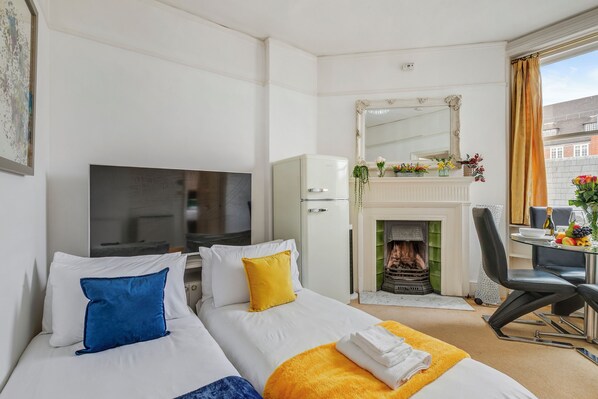 A hotel room with two beds, a TV, a fireplace, a dining table with chairs, and a view of the city.