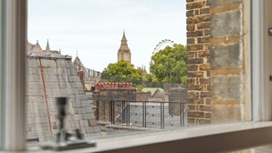 A view from a window overlooking a brick building with a clock tower in the distance.