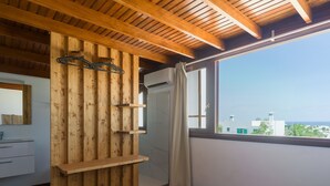 A bedroom with a wooden slat wall, a bed, a window with a view of buildings, and a bathroom with a shower.
