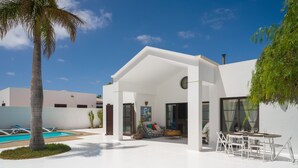 Een modern huis met een zwembad, terrasmeubilair buiten en een overdekt patio.