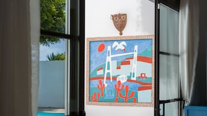 Een kamer met uitzicht op een zwembad, een kleurrijk abstract schilderij aan de muur en een bed met veel kussens.