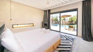Quarto moderno com cama grande, ventilador de teto e vista para área de piscina externa.
