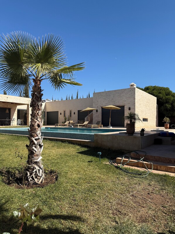 Une maison moderne dotée d’une piscine, d’un espace salon extérieur et d’un palmier.