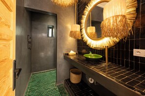 Une salle de bain avec un sol carrelé de carreaux verts, un lavabo noir avec un receveur vert, un miroir avec un cadre tressé et un porte-serviettes.