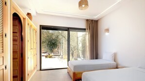 Quarto com duas camas, porta de correr para o exterior e portas de madeira à esquerda.