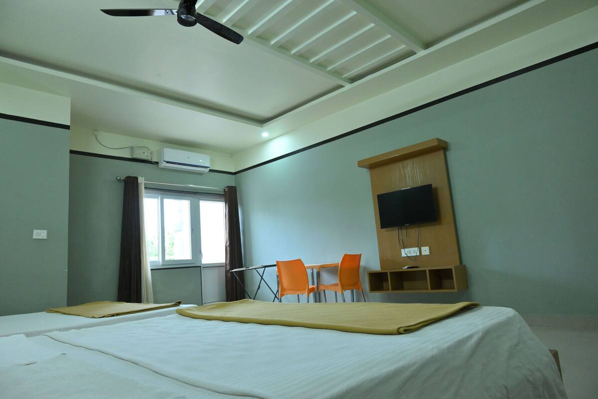 A hotel room with a bed, two chairs, a TV mounted on the wall, and a ceiling fan.