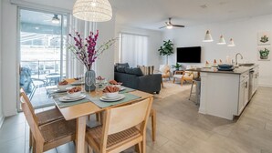 Une cuisine moderne dotée d’un îlot central, d’un coin repas avec une table pour quatre personnes et d’un salon avec un canapé et des fauteuils.