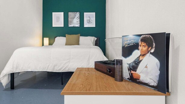 A bedroom with a bed, a bedside table with a radio, and a poster on the wall.