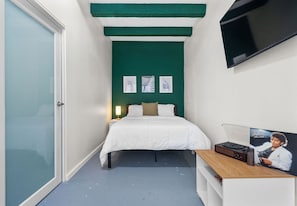 A bedroom with a bed, a TV mounted on the wall, and a poster on the nightstand.