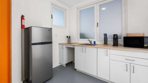 A compact kitchen with white cabinets, a stainless steel refrigerator, a microwave, and a coffee maker.