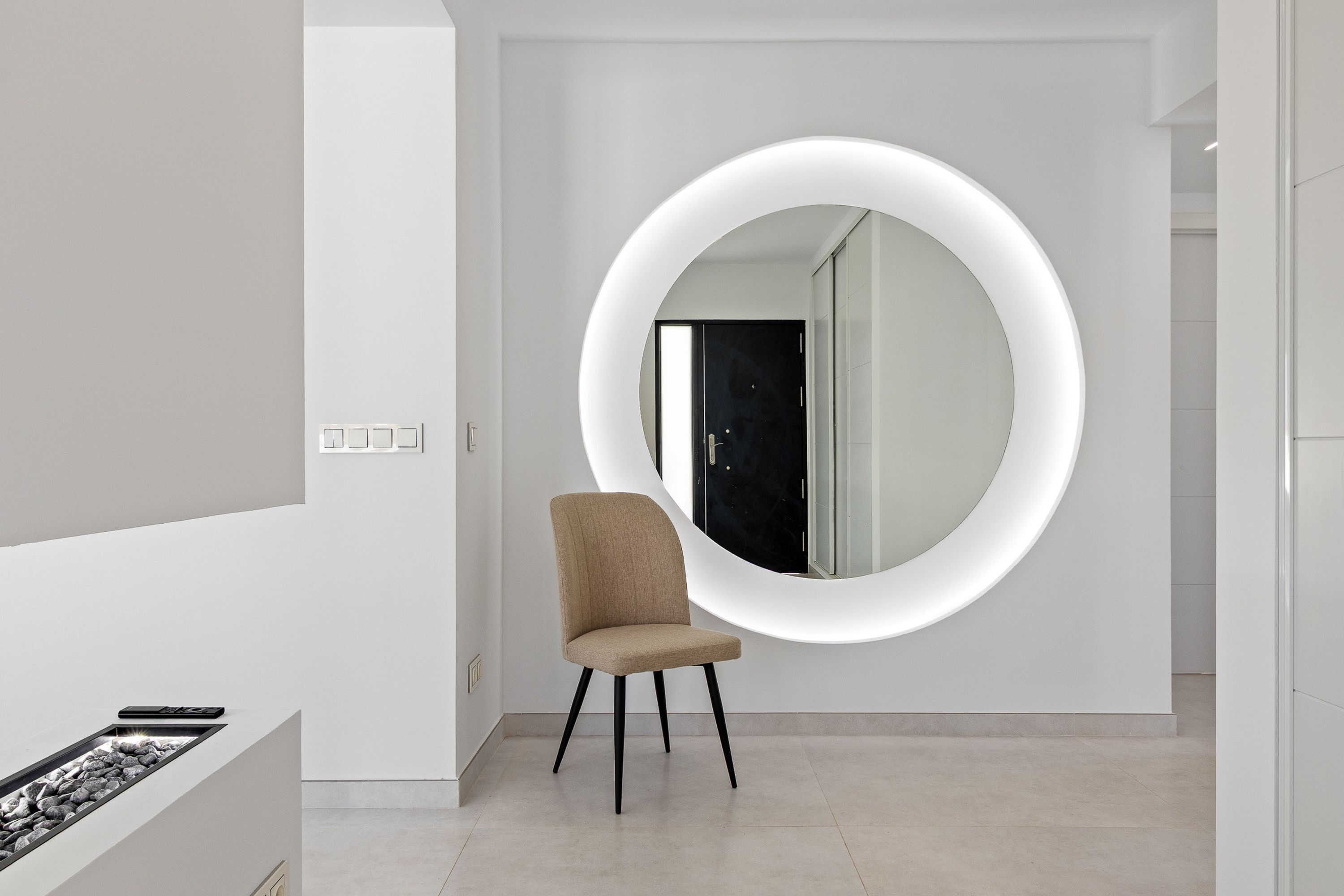 A modern interior with a round mirror, a beige chair, and a minimalist design.