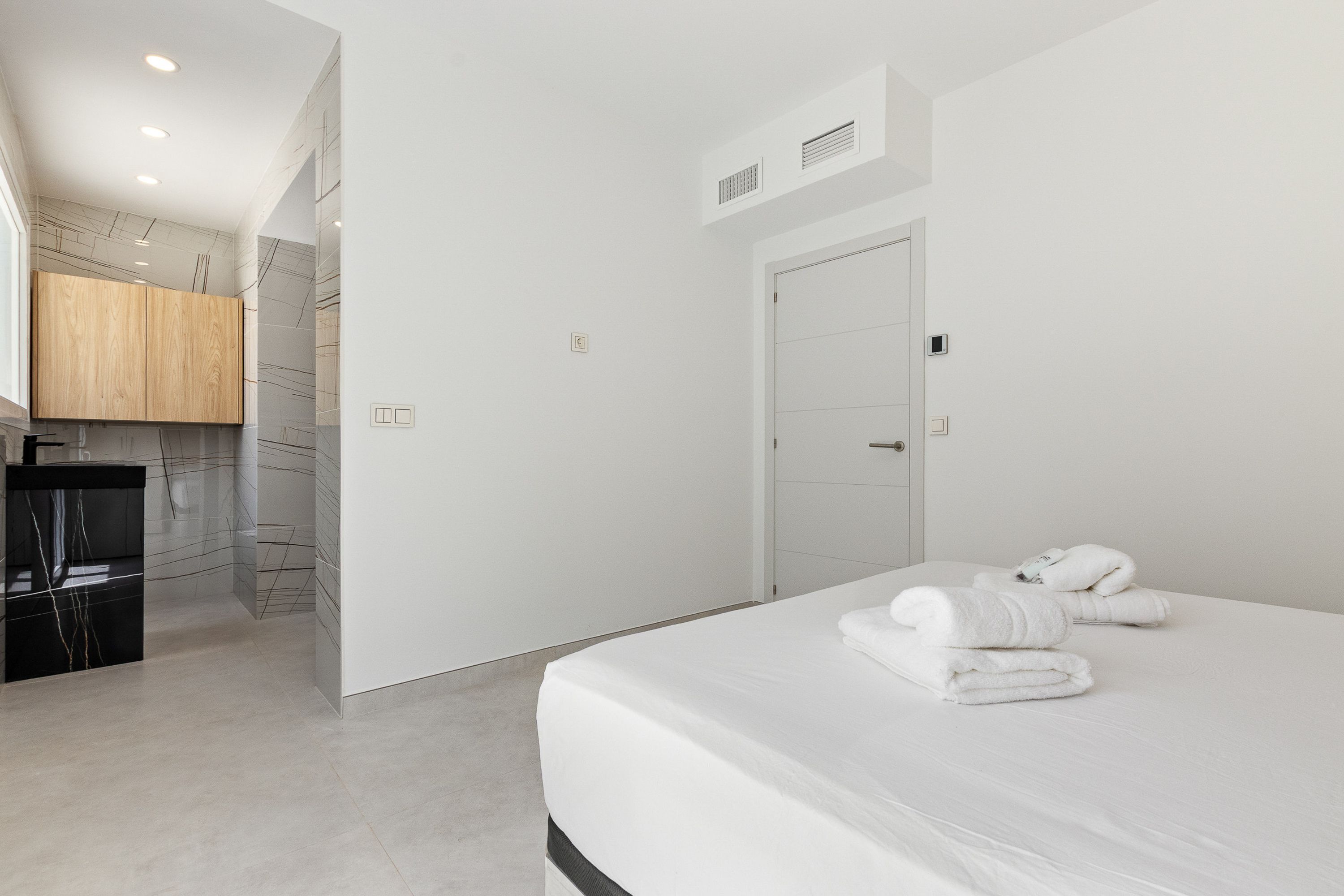 A modern hotel room with a large bed, a wooden cabinet, and a bathroom with a white door.