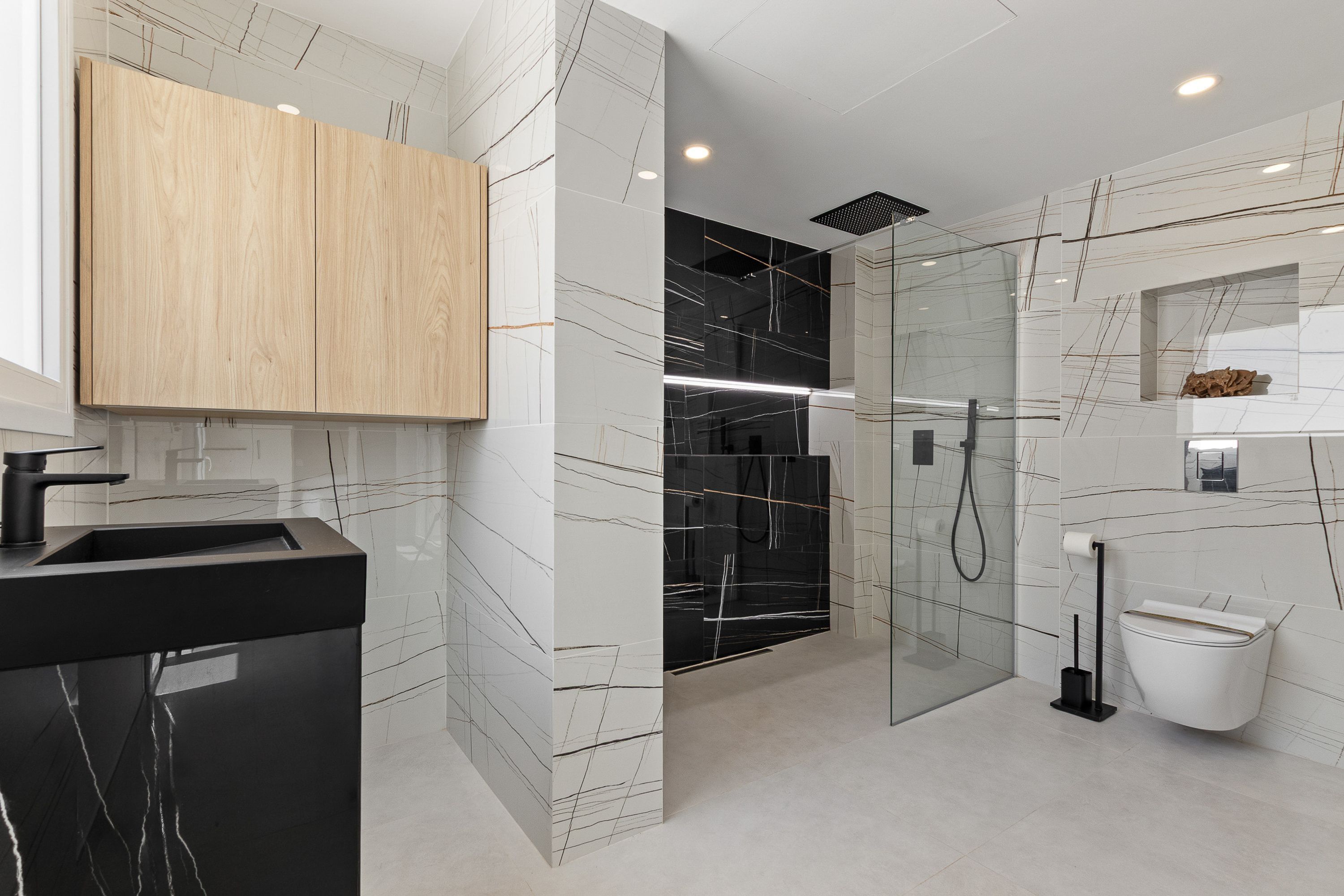 Une salle de bain moderne avec un lavabo noir, un meuble en bois et une douche séparée par des parois en verre.