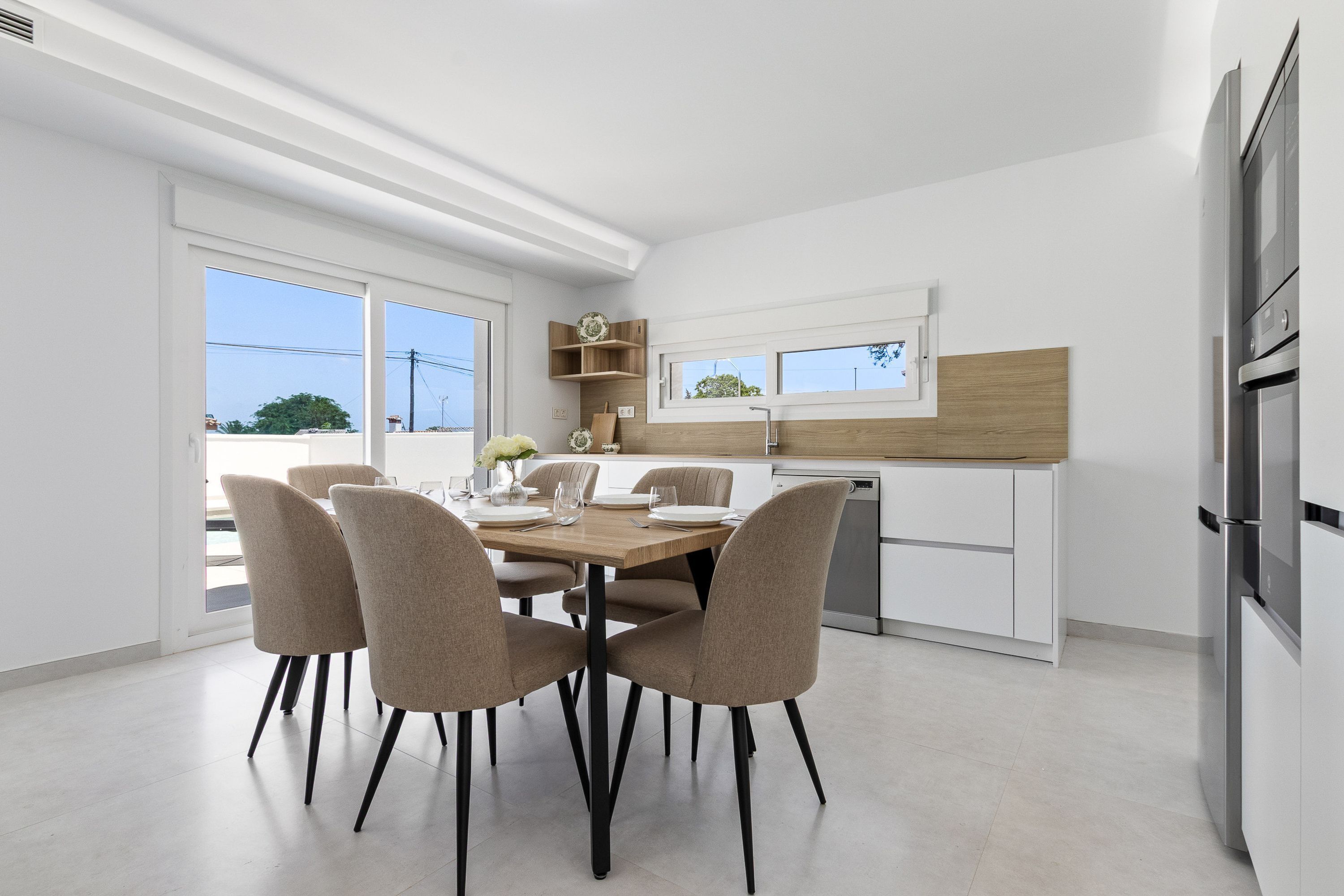 A modern kitchen with white cabinetry, a wooden dining table, and four chairs.