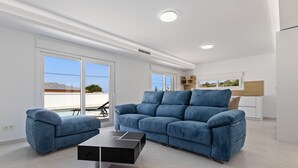 Una sala de estar moderna con un sofá azul, una mesa de centro negra y un comedor con una mesa y sillas de madera.