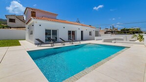 Una casa moderna con piscina, paredes exteriores blancas y tejado de tejas rojas.