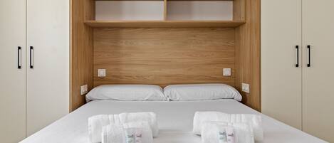 A bedroom with a wooden headboard, a bed with white linens, two towels, and toiletries.