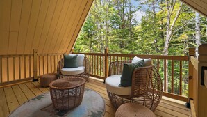 Una terraza de madera con mobiliario de mimbre y vista a un bosque.