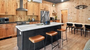 Una cocina moderna con armarios de madera, un refrigerador de acero inoxidable, una isla central con taburetes e iluminación colgante.